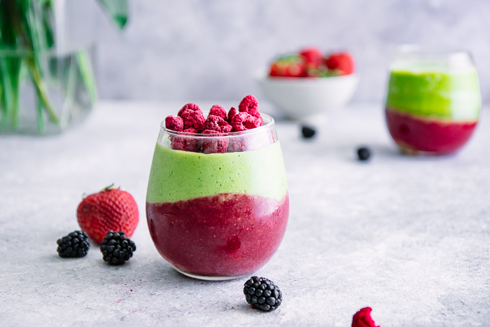 A green smoothie with avocado, spinach, banana, and raspberries on a white table with berries.