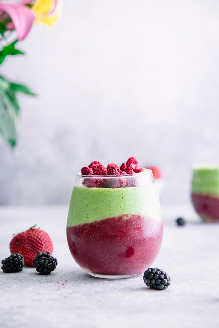 A green smoothie with avocado, spinach, banana, and raspberries on a white table with berries.