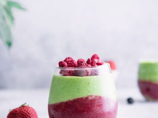 A green smoothie with avocado, spinach, banana, and raspberries on a white table with berries.