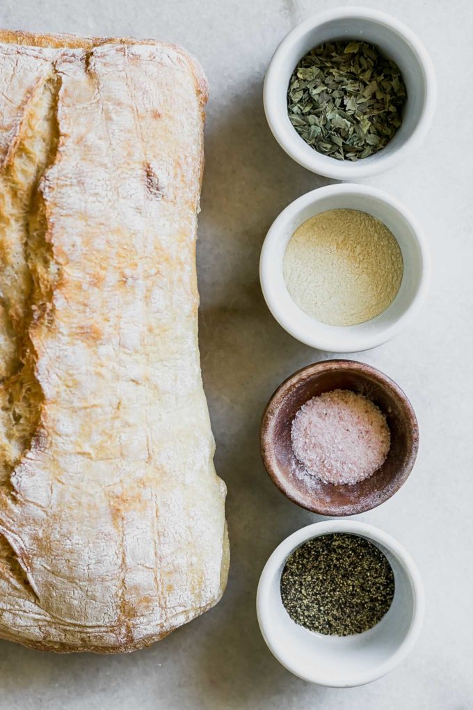 ciabatta bread and bowls of dried herbs, salt, pepper, and oil on a white table