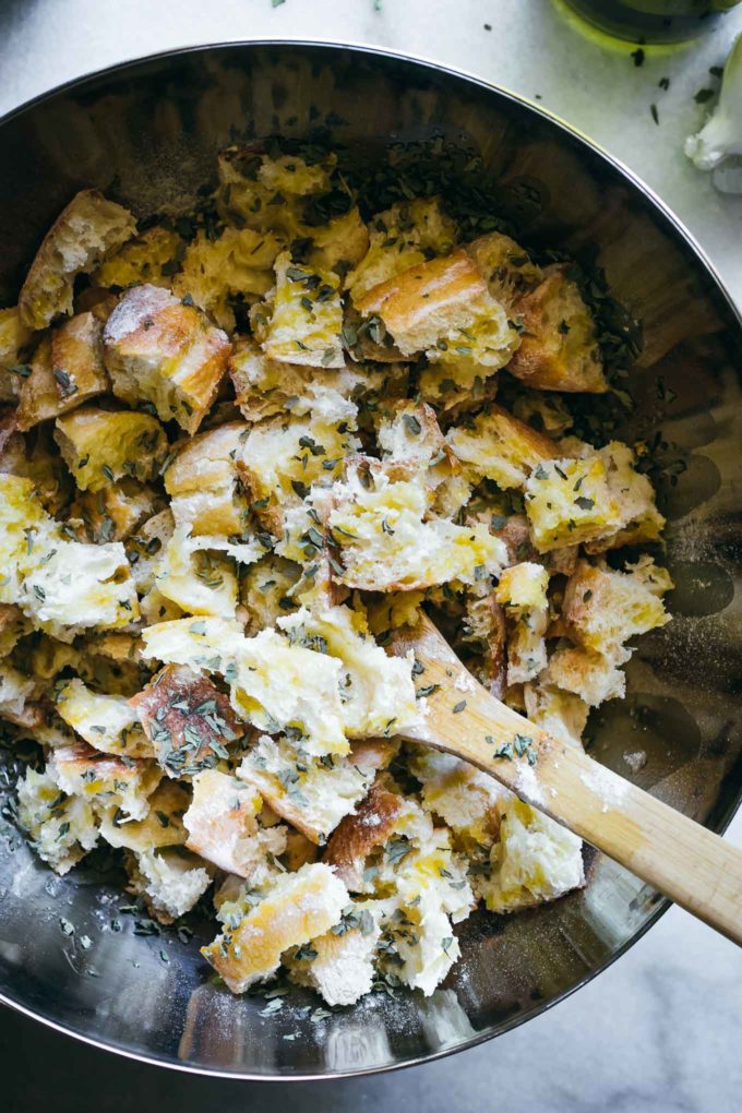 pieces of ciabatta bread inside a mixing bowl with oil and herbs