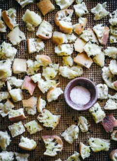 baked croutons made with ciabatta bread on a baking sheet with a bowl of salt