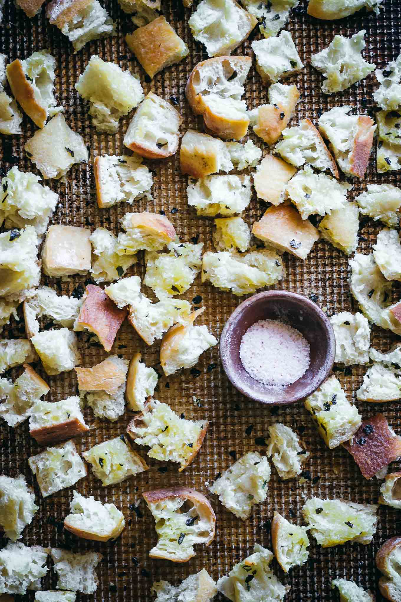 baked croutons made with ciabatta bread on a baking sheet with a bowl of salt