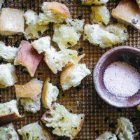 baked ciabatta croutons on a baking sheet with a bowl of salt