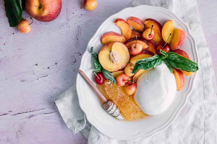 a peach and cherry fruit salad with basil, burrata cheese, and honeycomb