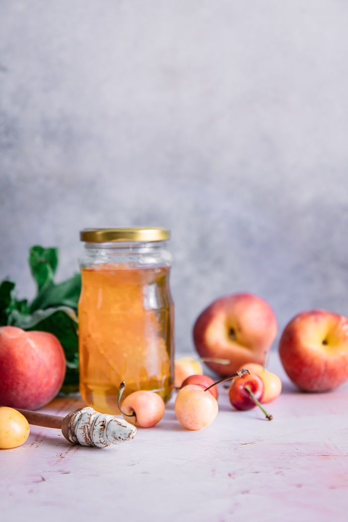 a jar of honeycomb on a pink table with whole peaches and cherries