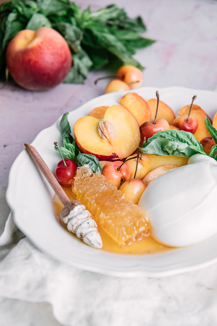 a peach honeycomb and burrata cheese fruit salad on a white plate
