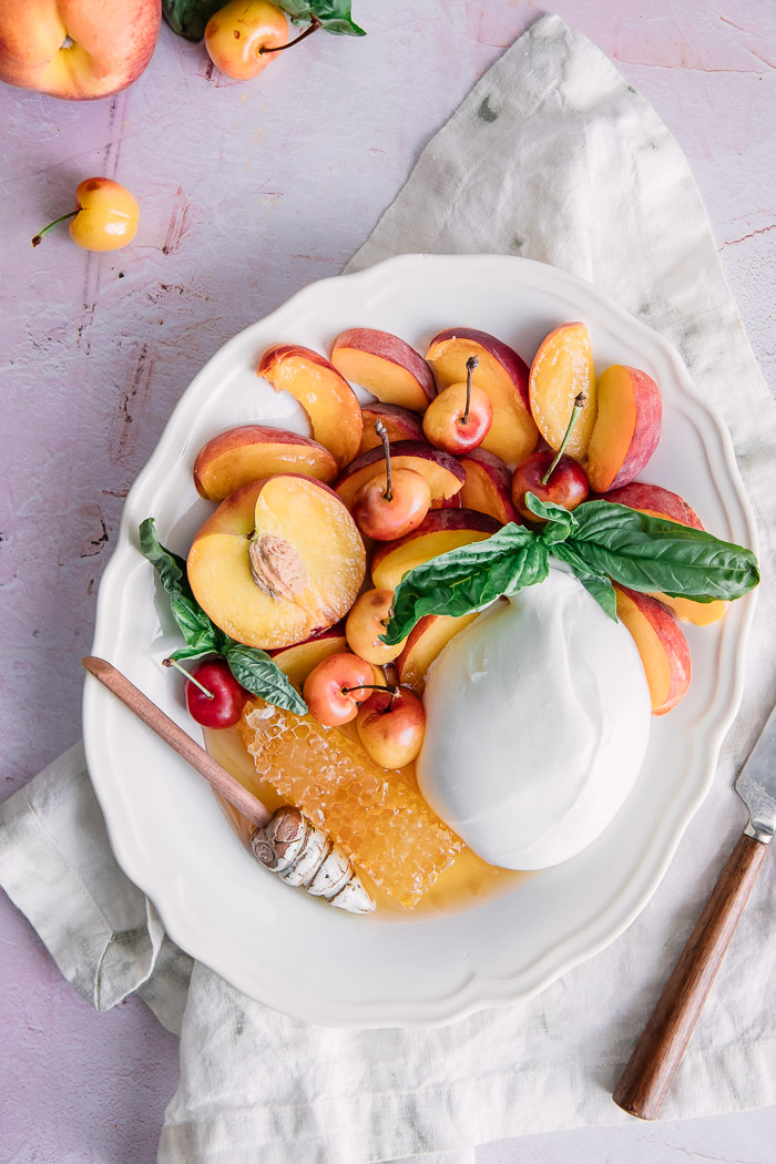 honeycomb, burrata cheese, and sliced fruit on a white plate