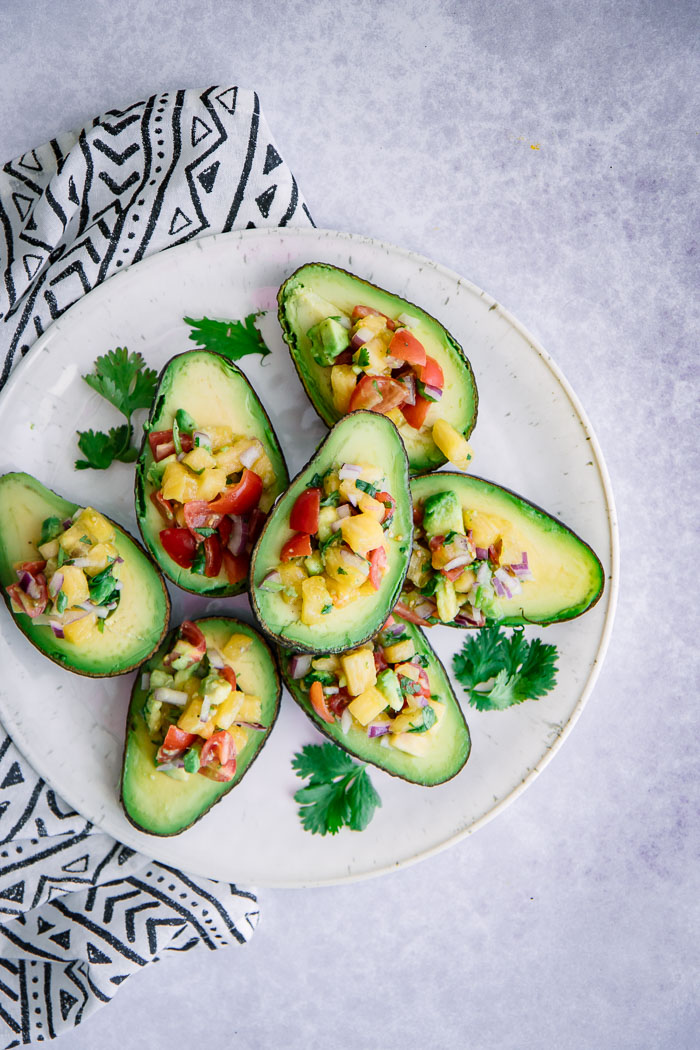 Pineapple pico de gallo inside of avocados on a white table with a black and white patterned napkin.