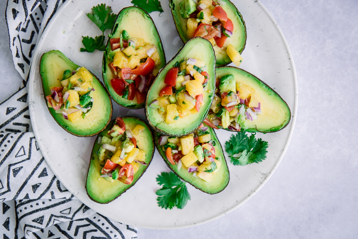 Avocado halves on a white plate with pineapple salsa inside.