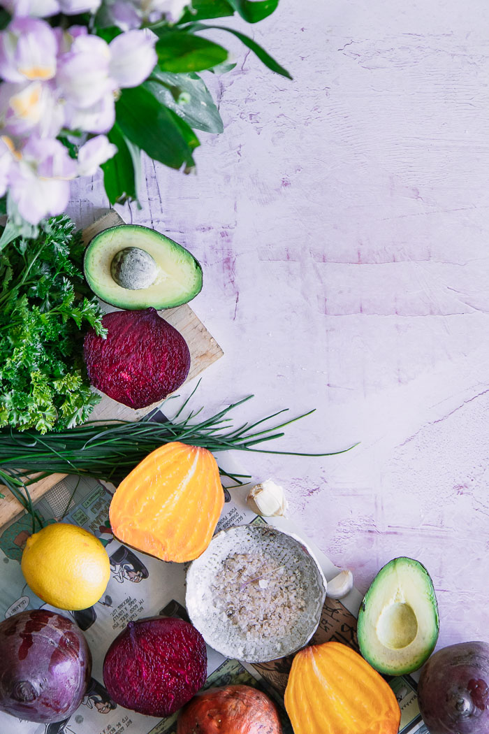 Beets, avocado, and herbs on a pink table.