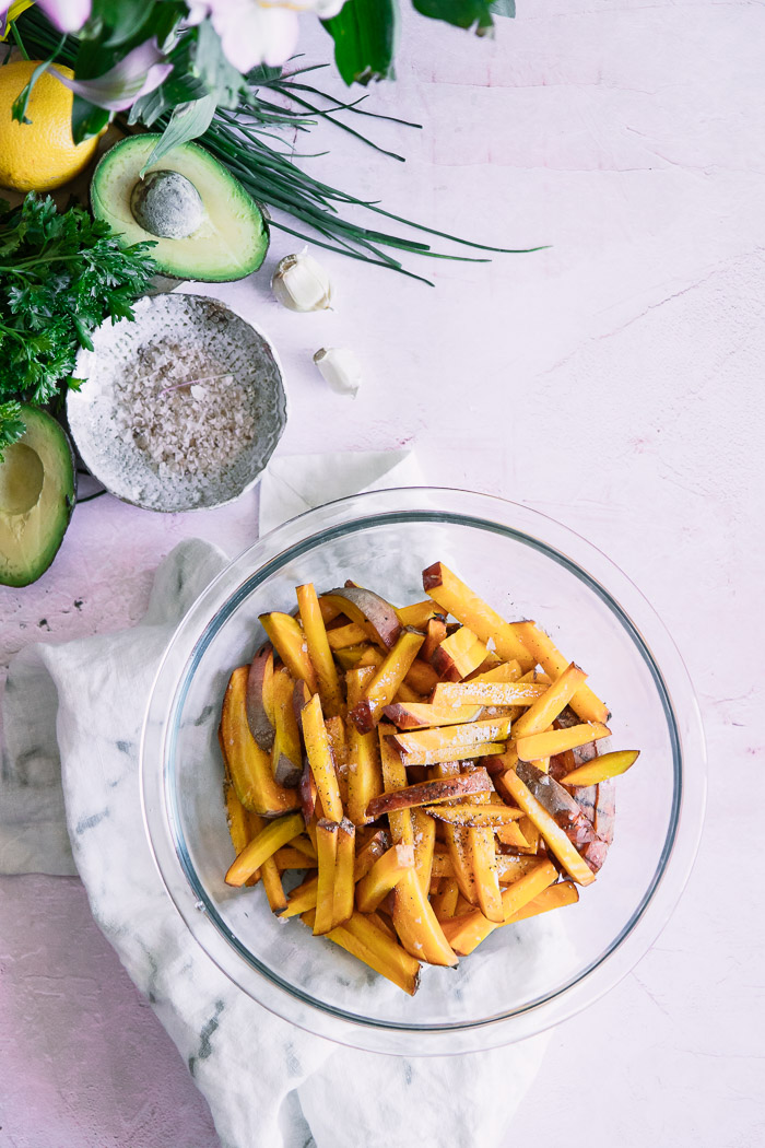 Cut golden beets in a bowl on a pink table with herbs and an avocado.