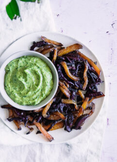 Roasted beet fries on a white plate with green dip on a pink table.