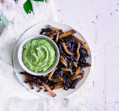 Roasted beet fries on a white plate with green dip on a pink table.