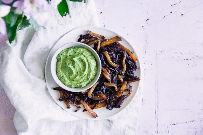 Roasted beet fries on a white plate with green dip on a pink table.