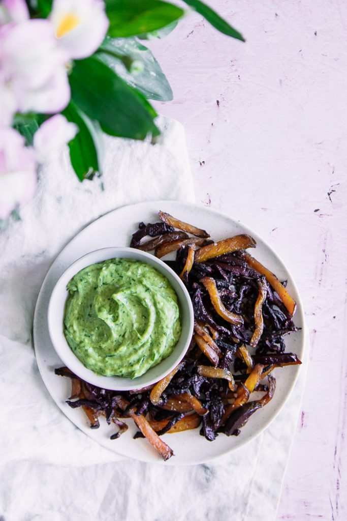 Roasted beets on a white plate with green dip on a pink table.