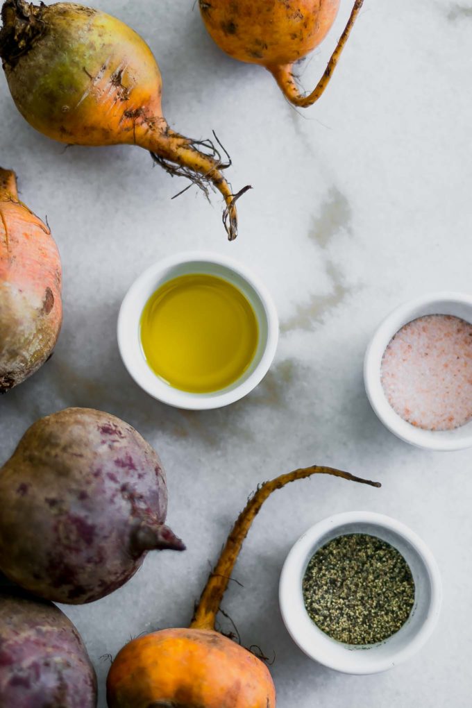 red and golden beets on a marble counter with bowls of oil, salt, and pepper