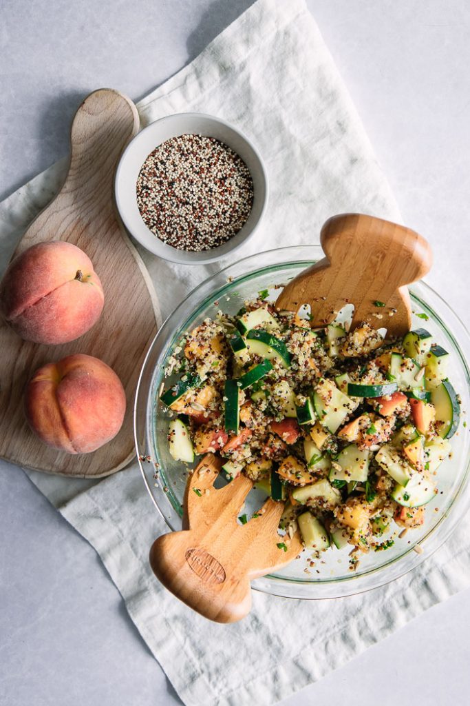 A large glass bowl with a peach and quinoa vegan salad with peaches on a cutting board.