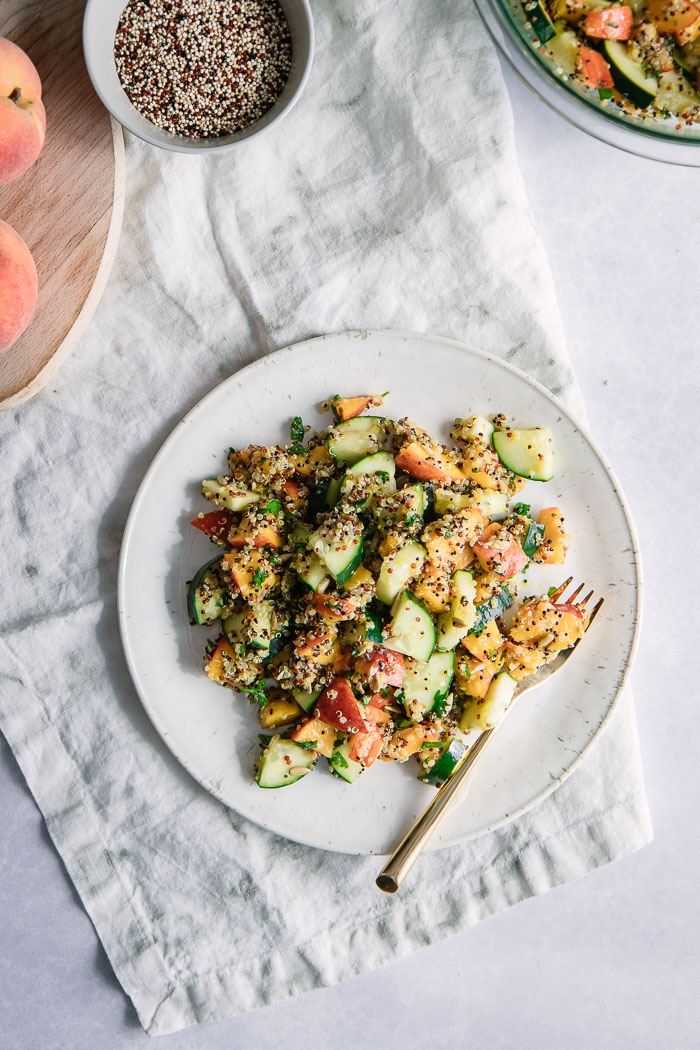 Fruit and grain salad with peaches and quinoa on a white plate on a white table.