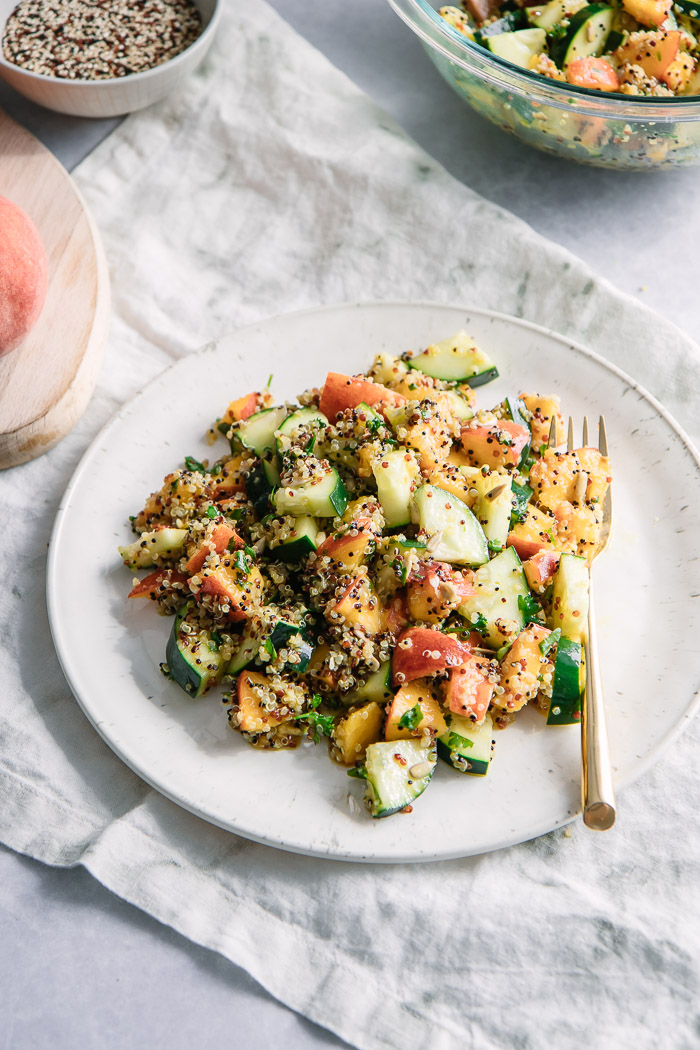 A vegan grain salad with fruit and vegetables on a white plate with a gold fork.