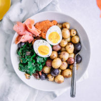A savory breakfast bowl with salmon, eggs, and potatoes on a white bowl.