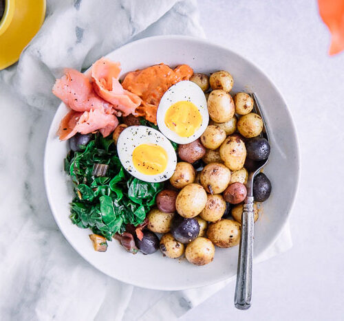 A savory breakfast bowl with salmon, eggs, and potatoes on a white bowl.