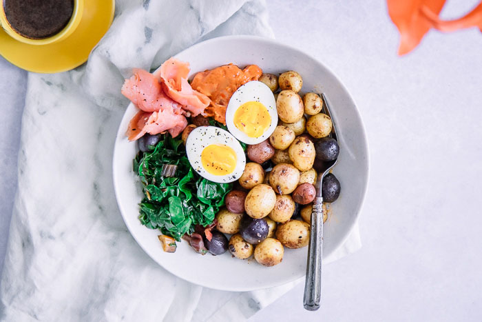 A savory breakfast bowl with salmon, eggs, and potatoes on a white bowl.