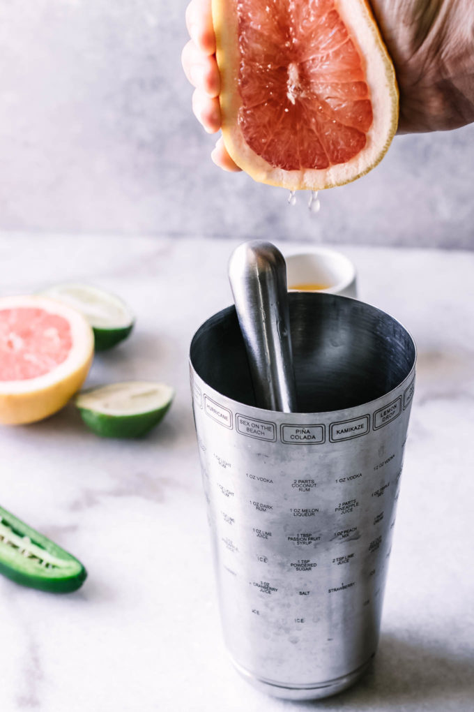 a hand squeezing grapefruit juice into a cocktail shaker