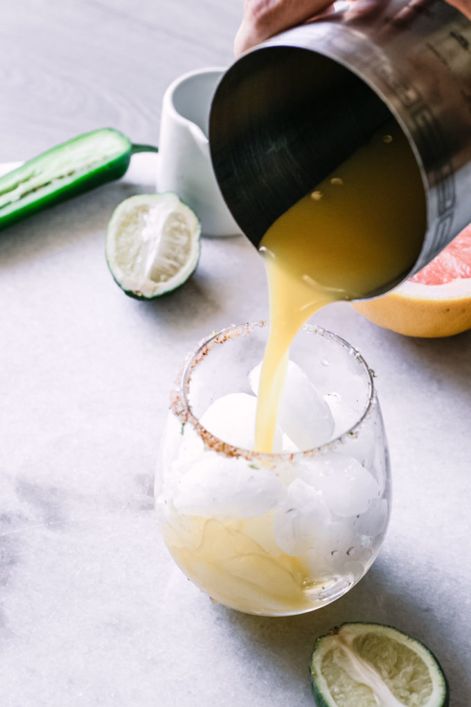 a hand pouring a grapefruit margarita into a glass