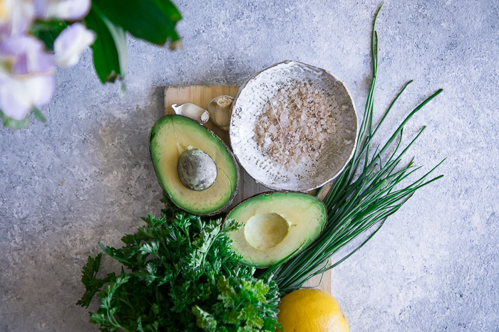 Avocados, salt, lemon, and fresh herbs on a cutting board.