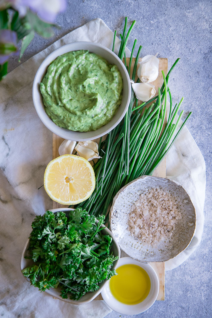 Green goddess dip on a cutting board with lemon, parsley, chives, and salt.