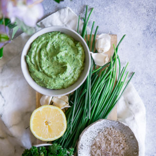 A white bowl with a bright green vegan dip on a blue table.