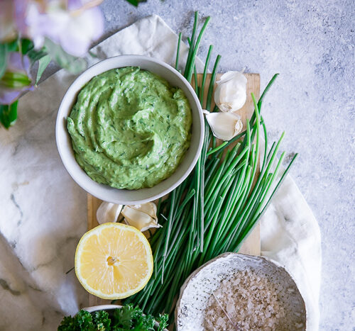 A white bowl with a bright green vegan dip on a blue table.