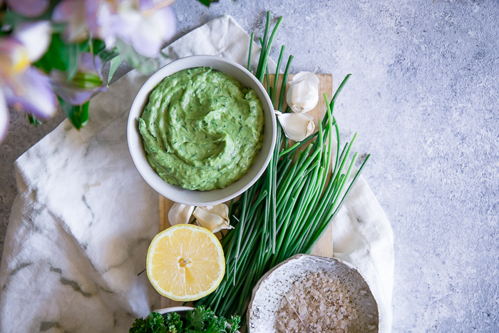 A white bowl with a bright green vegan dip on a blue table.