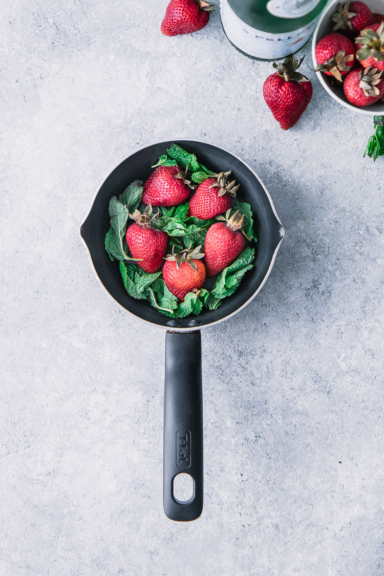 A small black saucepan filled with strawberries and mint.