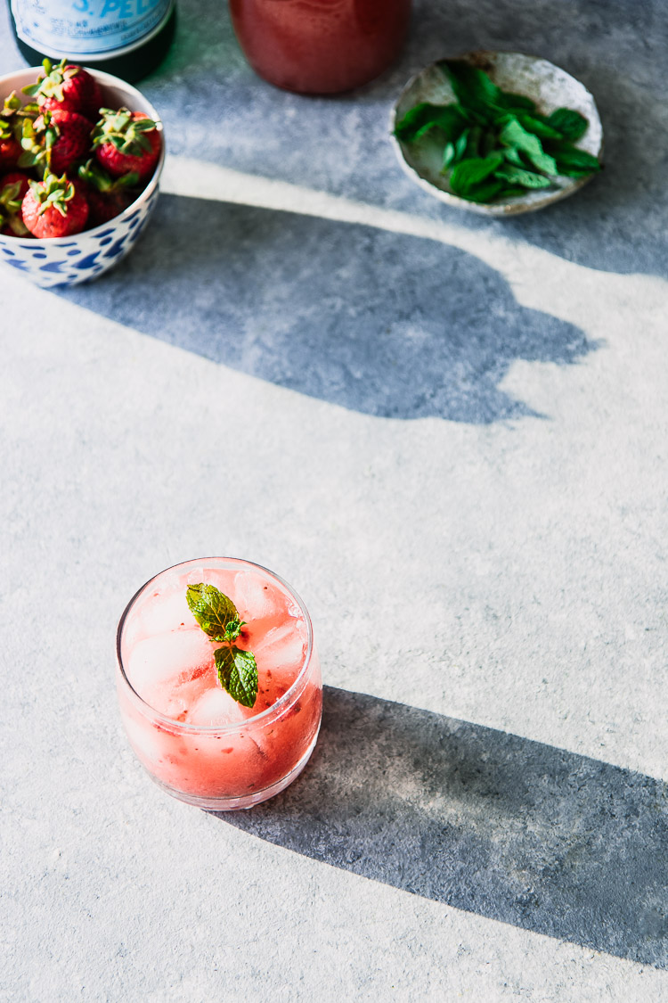 A pink sparkling water with strawberries and mint on a blue table.
