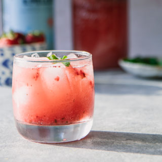 A glass of sparkling water with strawberries and mint on a blue table.