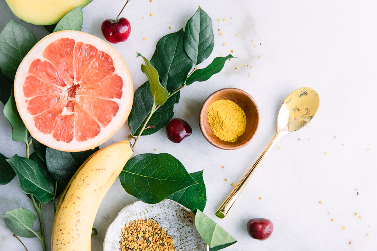 An arrangement of yellow superfoods including banana, grapefruit, bee pollen, mangos, and turmeric.