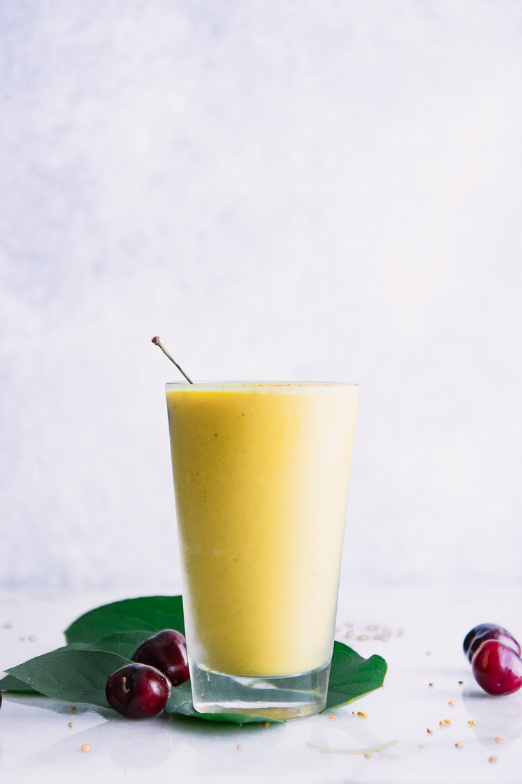 A ninety degree photo of a yellow mango banana smoothie in a glass with a white background.