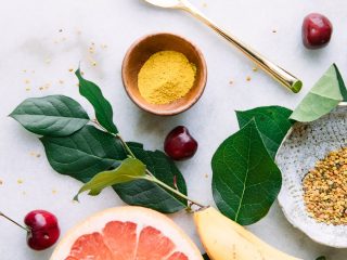 A flatlay of yellow superfoods including banana, grapefruit, turmeric, and bee pollen on a marble table.