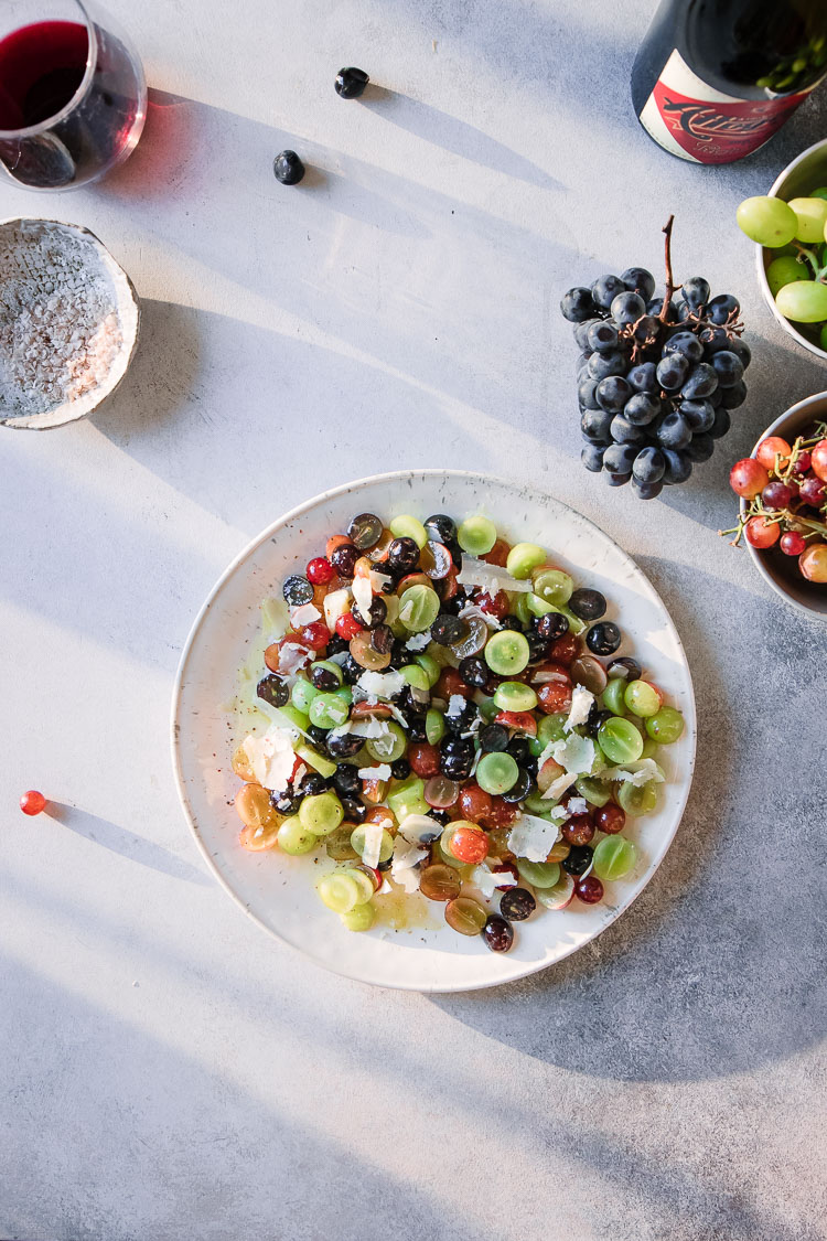 A grape and cheese fruit salad on a white plate on a white table with sunlight.