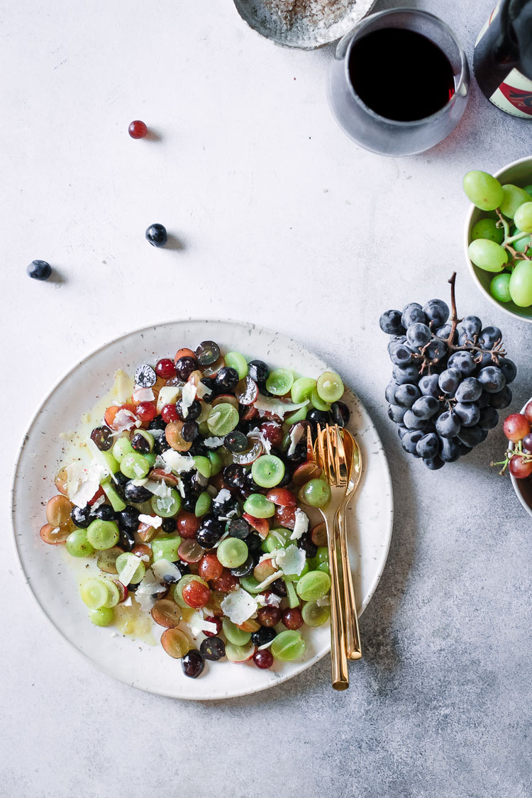 Red, green, and purple grapes with parmesan and olive oil on a white table.