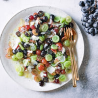 A mixed grape fruit salad on a white plate with gold silverware.