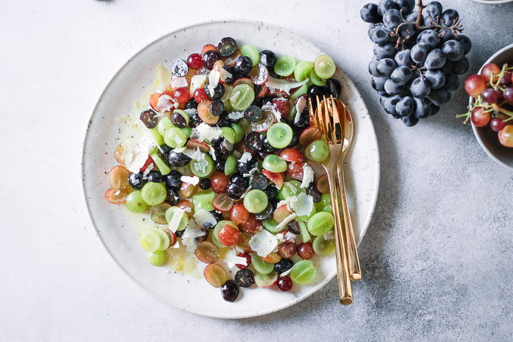 A mixed grape fruit salad on a white plate with gold silverware.