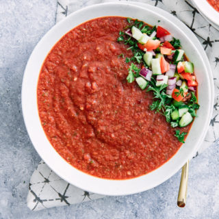 A close up photo of spicy tomato cucumber gazpacho on a blue table.