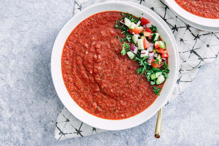 A close up photo of spicy tomato cucumber gazpacho on a blue table.