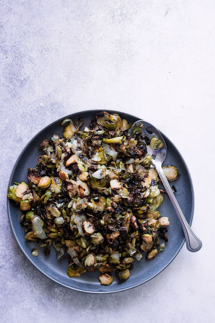 A blue plate with roasted brussels sprouts on a white table with a silver fork.