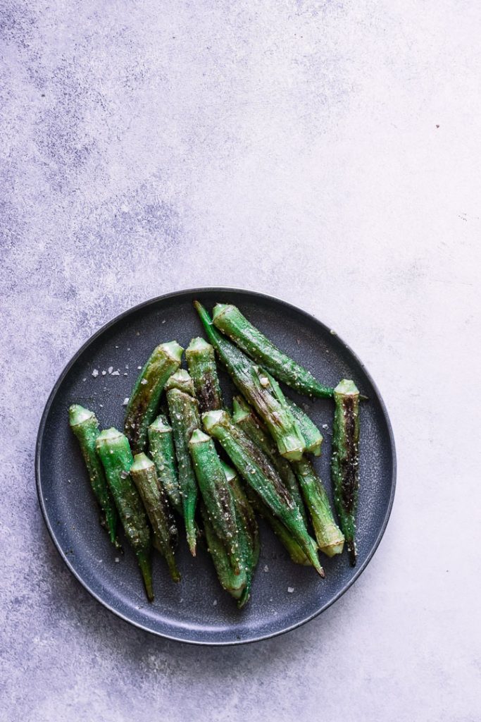 A dark plate with green okra on a white table.