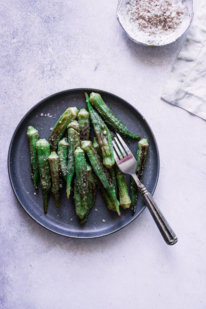 Pan fried okra on a blue plate with a silver fork.