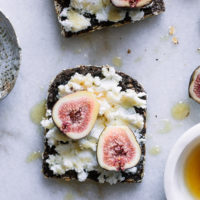 A piece of breakfast bread with cheese, figs, and honey on a table.